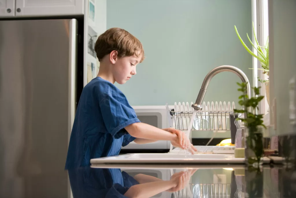 A child washing their hands at a kitchen sink