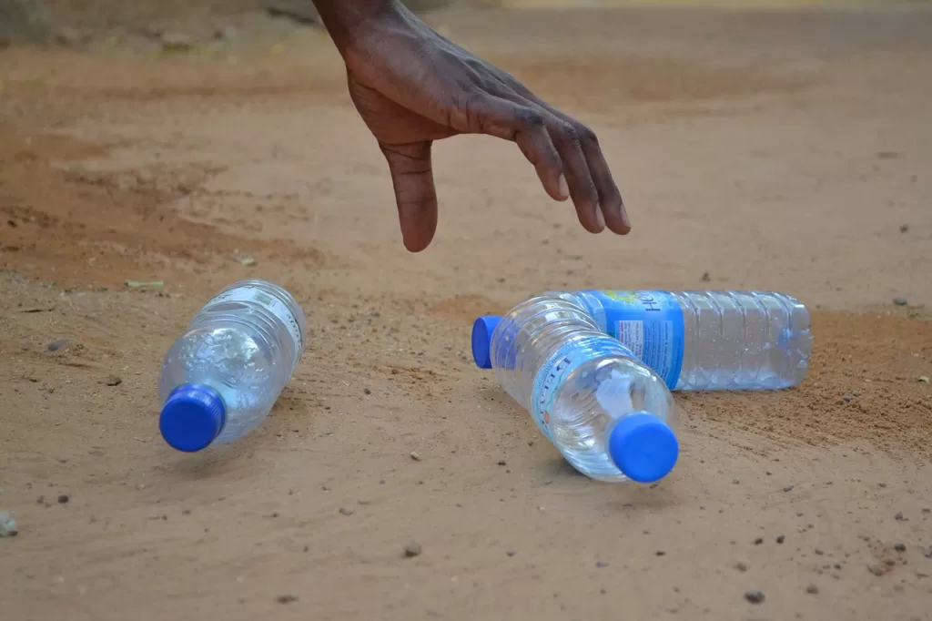 The hand of someone picking up empty plastic water bottles from a beach